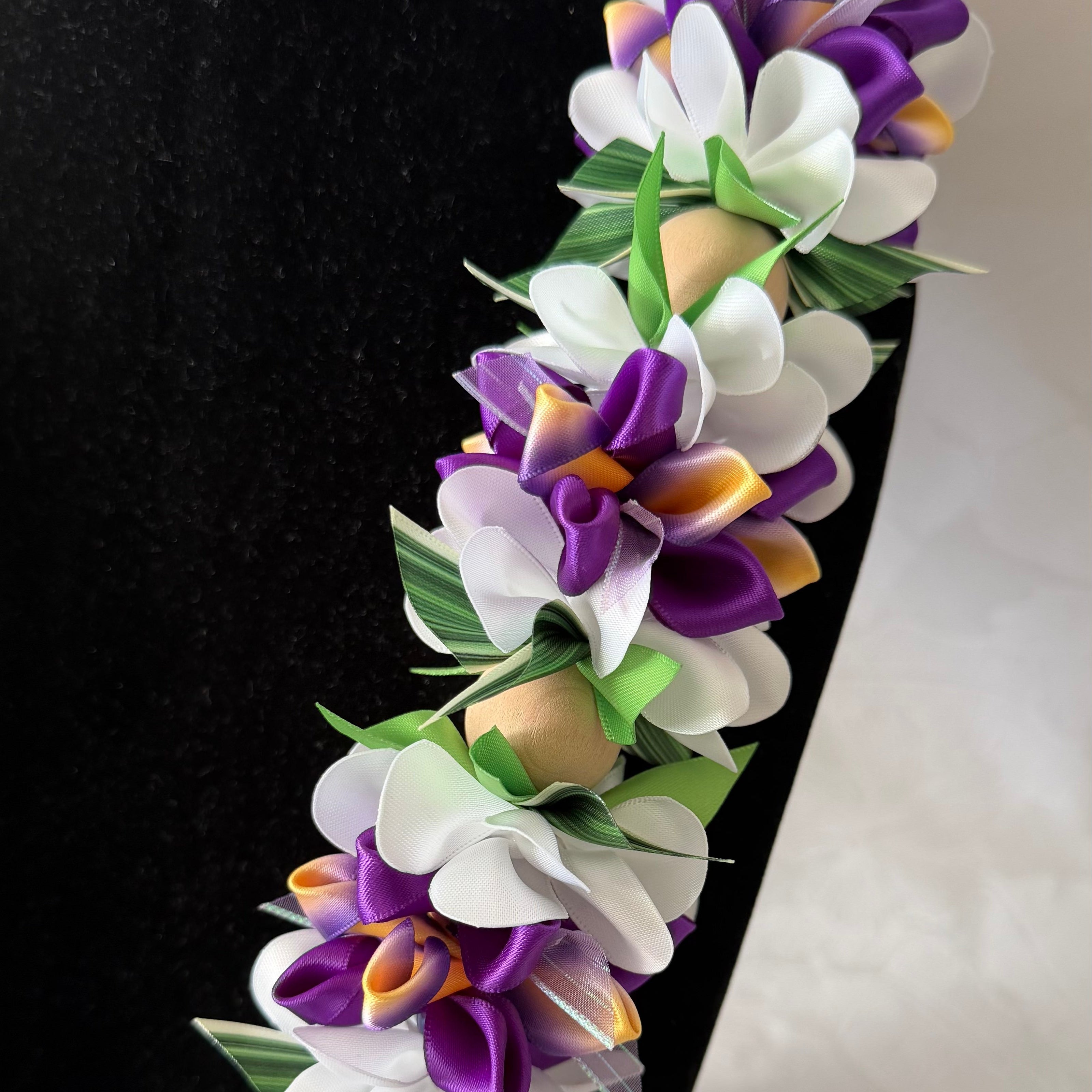 Floral lei with purple, white, and green flowers on a black stand.